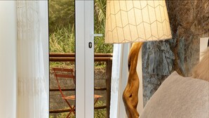 A room with a view of a wooden chair outside, a lamp, and a textured wall. - King Shelter by Homie (Porto Moniz)
