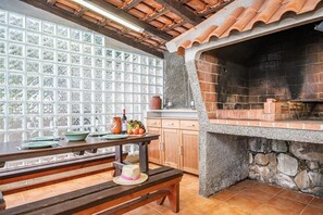 A kitchen with a stone oven, wooden cabinets, and a large window with a view of trees. - King Shelter by Homie (Porto Moniz)