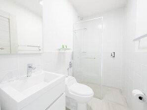 Un baño moderno con lavamanos, inodoro y zona de ducha blancos.