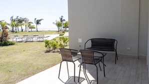 A patio with two wicker chairs and a table, overlooking a pool area with lounge chairs and palm trees. - Residences C7-pbb in Chame (Punta Chame)