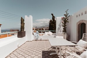 Une terrasse sur le toit, dotée d’un sol carrelé, de meubles blancs et offrant une vue sur la ville et les montagnes.