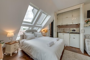 A bedroom with a large bed, a nightstand, a lamp, and a view of the sky through skylights.