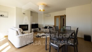 A modern living room with a sofa, TV, and dining area with chairs and a table. - Belle Vue Apartment by Acasadascasas (Mafra)