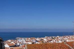Eine Küstenstadt mit weißen Häusern und roten Ziegeldächern, strahlend blauem Himmel und dem Meer im Hintergrund.