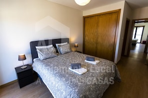 A bedroom with a large bed, two bedside tables, a wooden wardrobe, and a nightstand with a lamp.