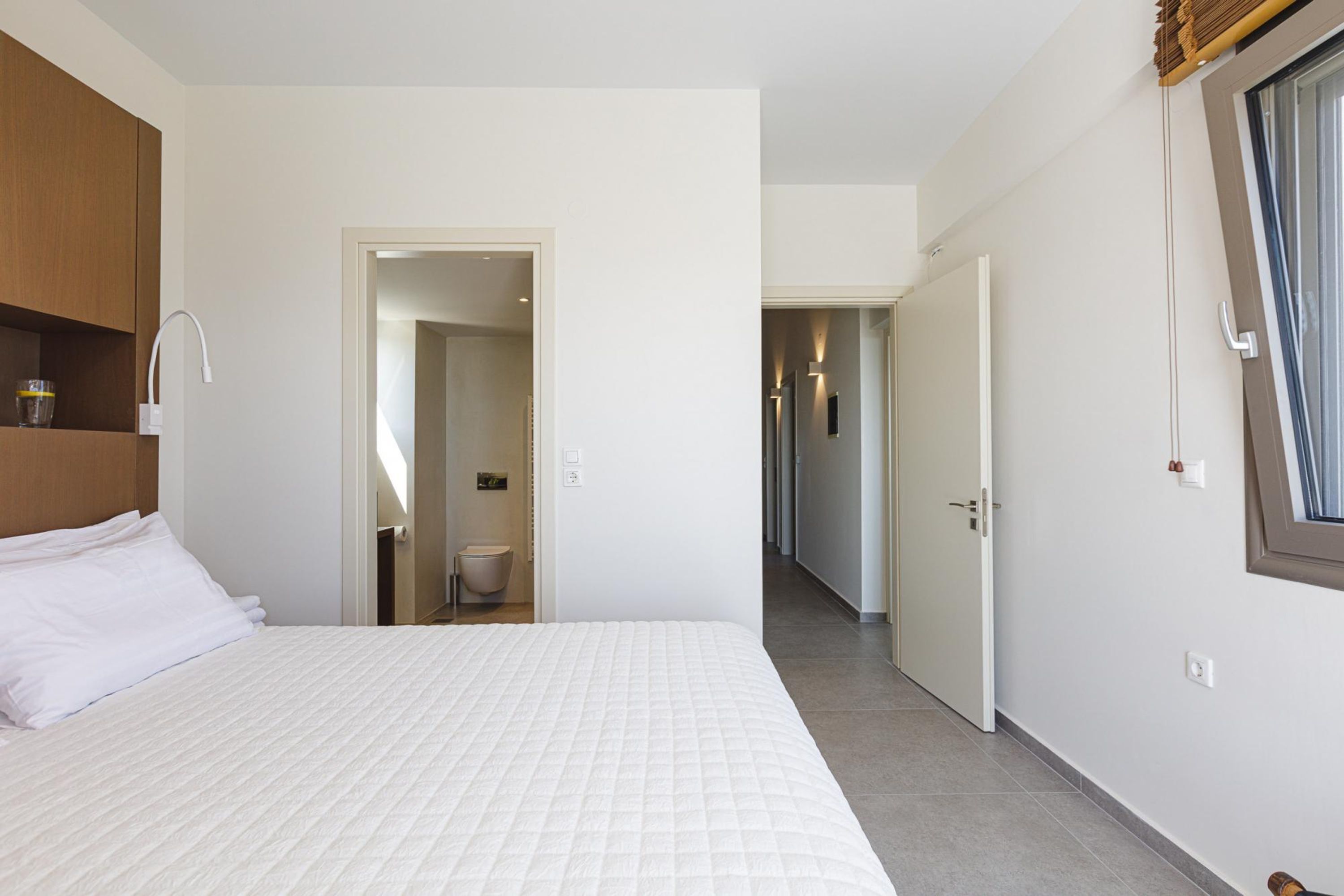 Une chambre à coucher avec un grand lit, une tête de lit en bois, une table de chevet avec une lampe et une fenêtre avec des rideaux.