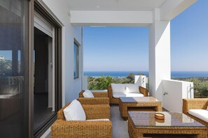 A balcony with wicker furniture and a glass table, overlooking a scenic view. - Villa Rizes Luxury in Maroulas (Rethymno)