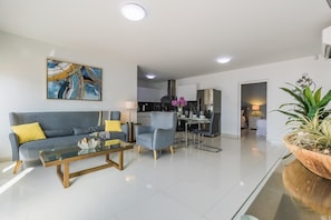 A modern living room with a sofa, coffee table, and dining area. - Koyari Modern Condos 1 (Noord)