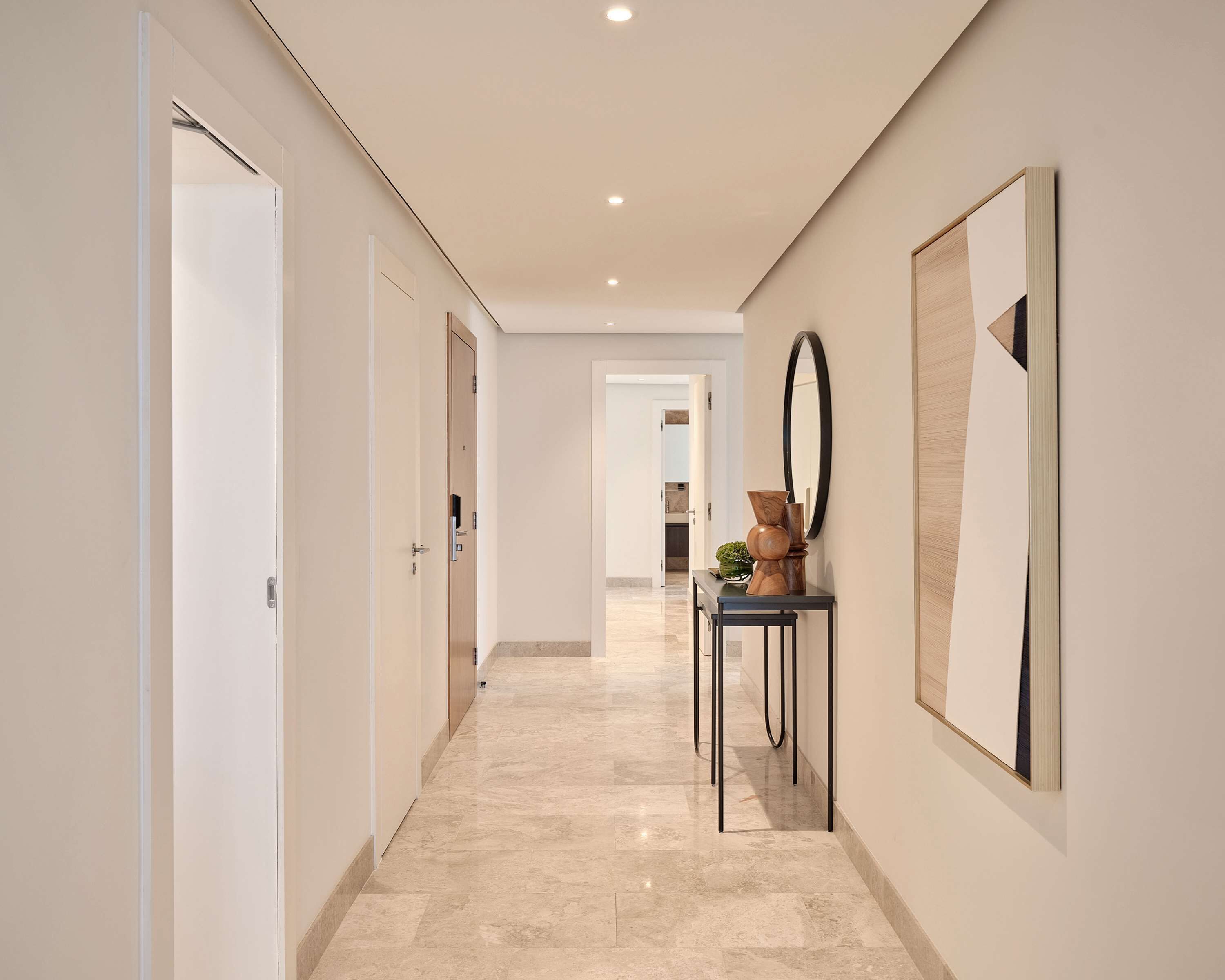 A hallway with a marble floor, white walls, and a black console table with decorative items.