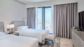 Una habitación de hotel moderna con dos camas, un ventanal con cortinas, un escritorio con lámpara y un televisor.