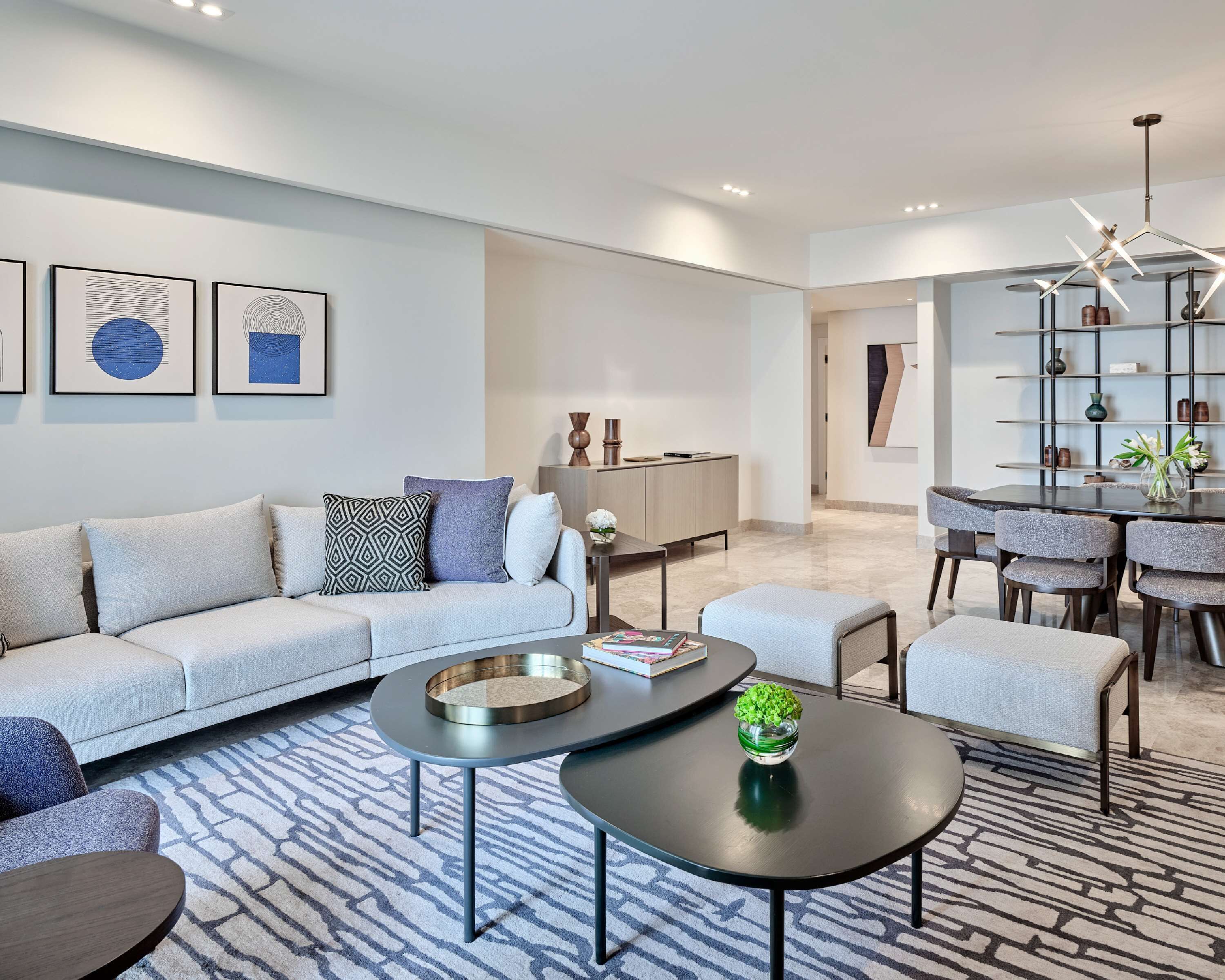 A modern living room with a sofa, coffee table, and ottoman. There is a dining area with a table and chairs.