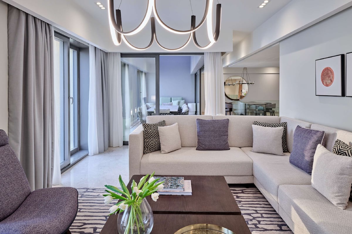 A modern living room with a sectional sofa, a coffee table with a vase of flowers, and a large window with curtains.