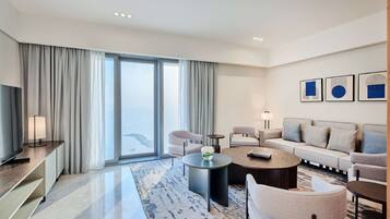 A modern hotel room with a large window, a sofa, a coffee table, a TV, and a lamp.