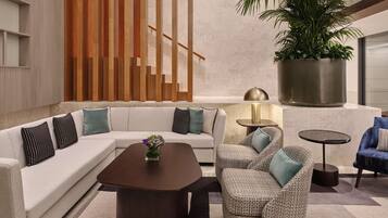 A modern lounge area with a sectional sofa, a patterned armchair, a coffee table, and a small round table with a lamp.