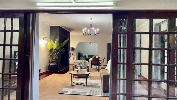 A spacious living room with a large TV, a chandelier, and a dining area. - Cozy 3 Bedroom House With Unique Bathrooms - 2084 (Bulawayo)