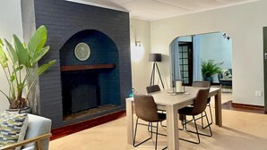 A dining area with a brick fireplace, a dining table with four chairs, and a potted plant. - Cozy 3 Bedroom House With Unique Bathrooms - 2084 (Bulawayo)