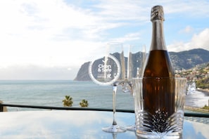 Ein Tisch mit einer Champagnerflasche und zwei Gläsern, vor einer malerischen Küstenlandschaft.
