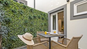 A patio with wicker chairs, a table, and a green vertical garden wall. - Funchal Tropical - Hurricane Plant by Homie (Funchal)