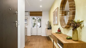 A hallway with wooden flooring, a wooden bench, a mirror, and a vase with flowers. - Funchal Tropical - Hurricane Plant by Homie (Funchal)