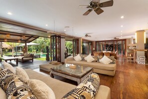 Relax in a spacious living area with a sofa set, coffee table, and balcony overlooking a lush garden and pool.