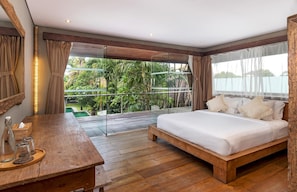 Relax in a serene bedroom with a large bed overlooking lush greenery and a body of water.