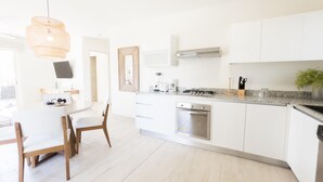 A modern kitchen with white cabinetry, a built-in oven, a gas stove, and a dining area with a table and chairs. - Residences C12-pbb in Chame (Punta Chame)