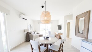 A modern living room with a sofa, a dining table with chairs, a TV mounted on the wall, and a large mirror. - Residences C12-pbb in Chame (Punta Chame)