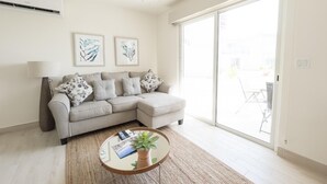 A modern living room with a grey sectional sofa, a round coffee table with a plant, and a ceiling fan. There are two framed artworks on the wall and a large sliding glass door to the right. - Residences C12-pbb in Chame (Punta Chame)