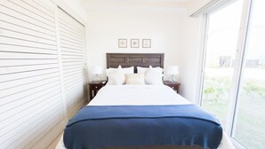 A bedroom with a large bed, white walls, a wooden headboard, and a view of the outdoors through a large window. - Residences C12-pbb in Chame (Punta Chame)