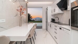 A modern kitchen with a marble countertop, white cabinetry, and a view of a sunset over a body of water.