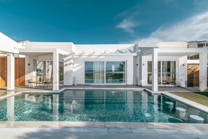 A modern house with a swimming pool, large glass doors, and a pergola.