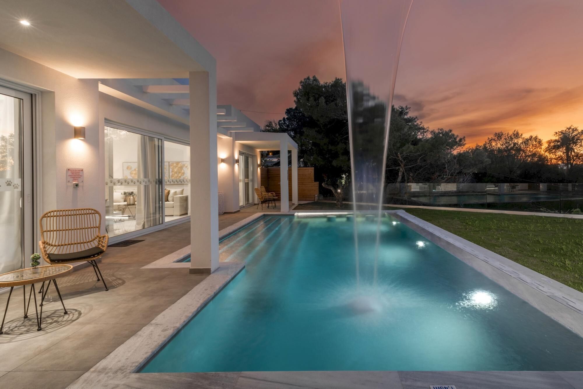 A modern outdoor pool area with a clear view of the sky at dusk, a wooden deck, and a lounge chair.