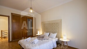 A bedroom with a large bed, a wooden headboard, two bedside tables with lamps, and a hanging light fixture.
