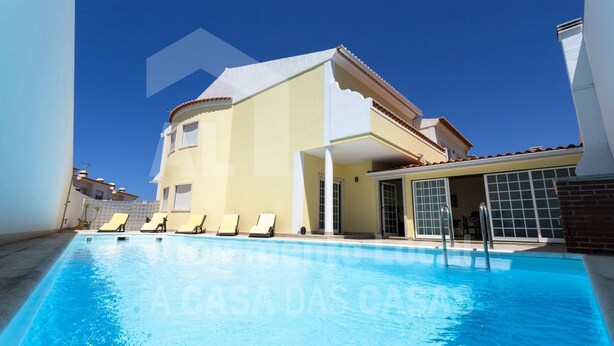 A poolside view of a two-story building with a flat roof, a covered patio area, and a clear blue sky.