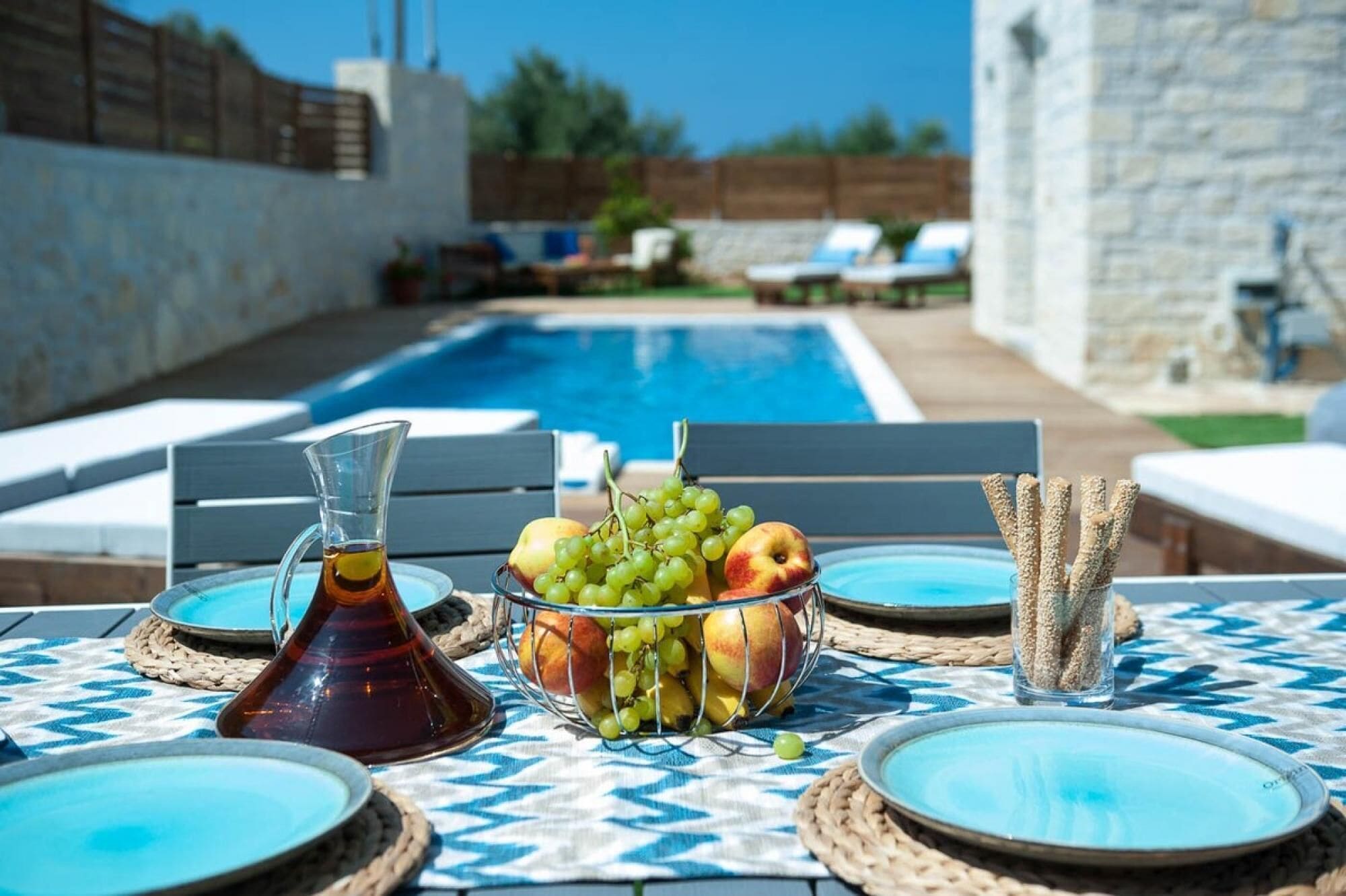 A poolside table with a fruit bowl, a pitcher, and a glass of water.