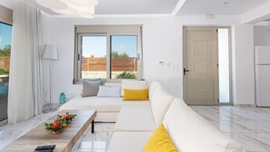 A modern living room with a sofa, a coffee table with flowers, a lamp, and a view of the outside. - Villa Prima - With Private Heated Pool (Rethymno)