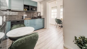 Una cocina moderna con armarios azul verdoso, encimera de mármol y comedor con una mesa redonda y sillas verdes.