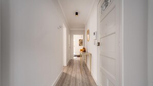 Un pasillo con suelo de madera, paredes blancas y una puerta a la derecha.
