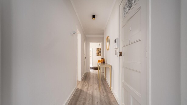 Un couloir avec un plancher en bois, des murs blancs et une porte sur le côté droit.