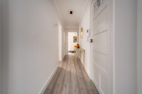 Un couloir avec un plancher en bois, des murs blancs et une porte sur le côté droit.