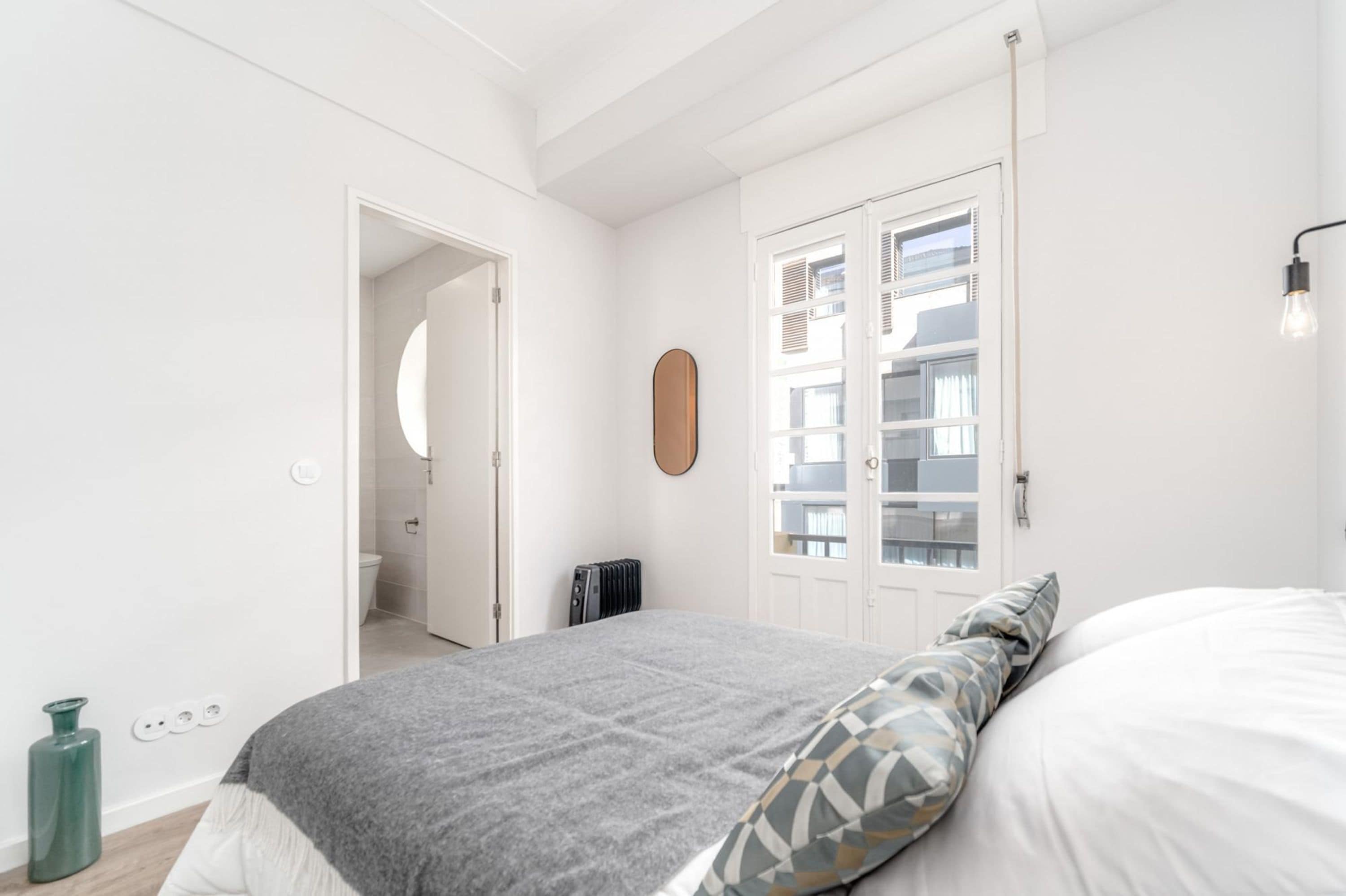 Quarto com cama, radiador, porta e luminária fixada na parede.