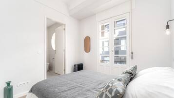 Quarto com cama, radiador, porta e luminária fixada na parede.