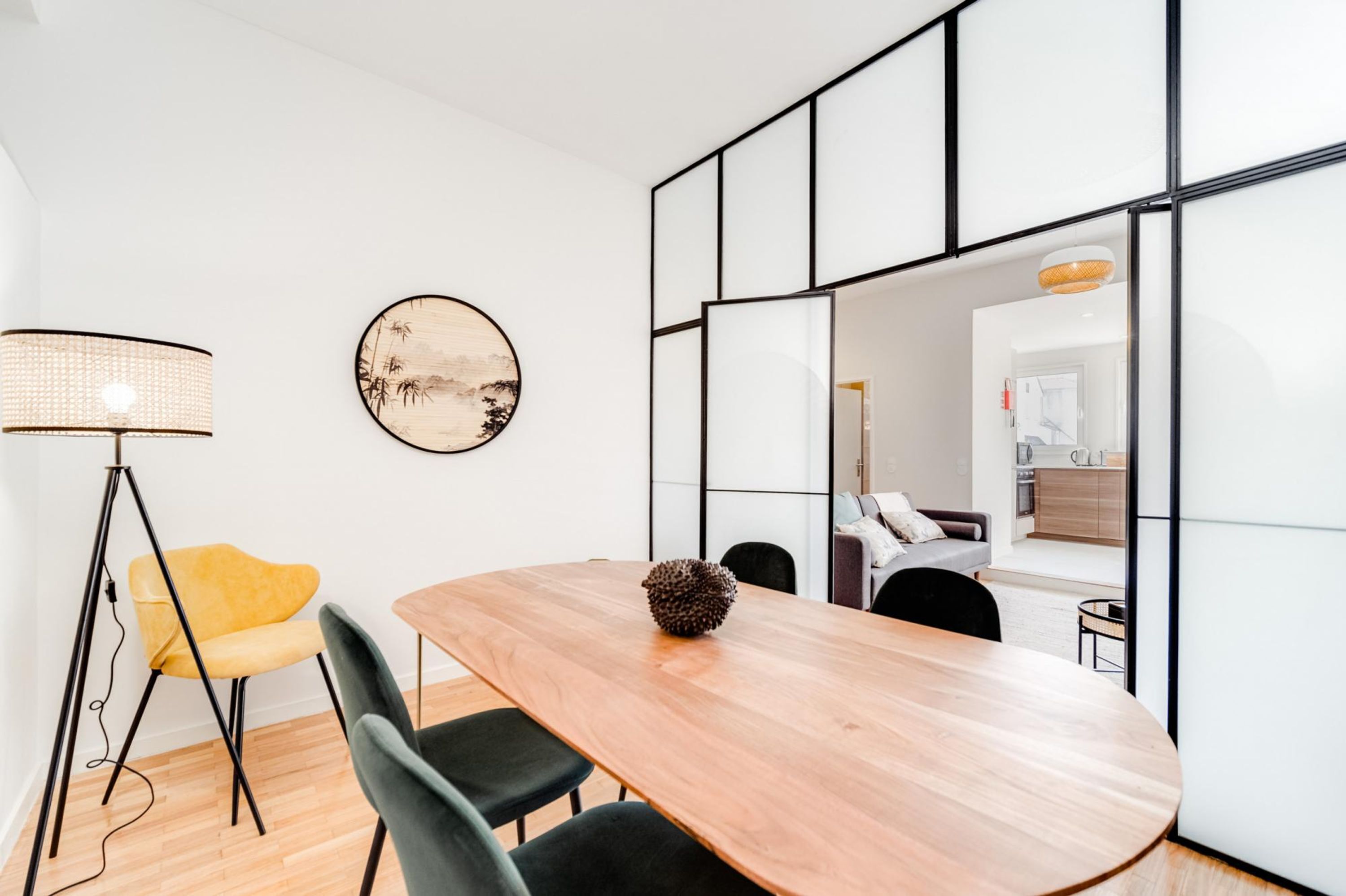 Uma área de jantar moderna com uma mesa de madeira, cadeiras pretas, uma cadeira amarela, um abajur e um objeto decorativo sobre a mesa.