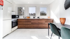A modern kitchen with white cabinets, a wooden countertop, and a dining area with a green chair. - Nomad s By Sta Catarina Flats - 3bdr Family (Porto)