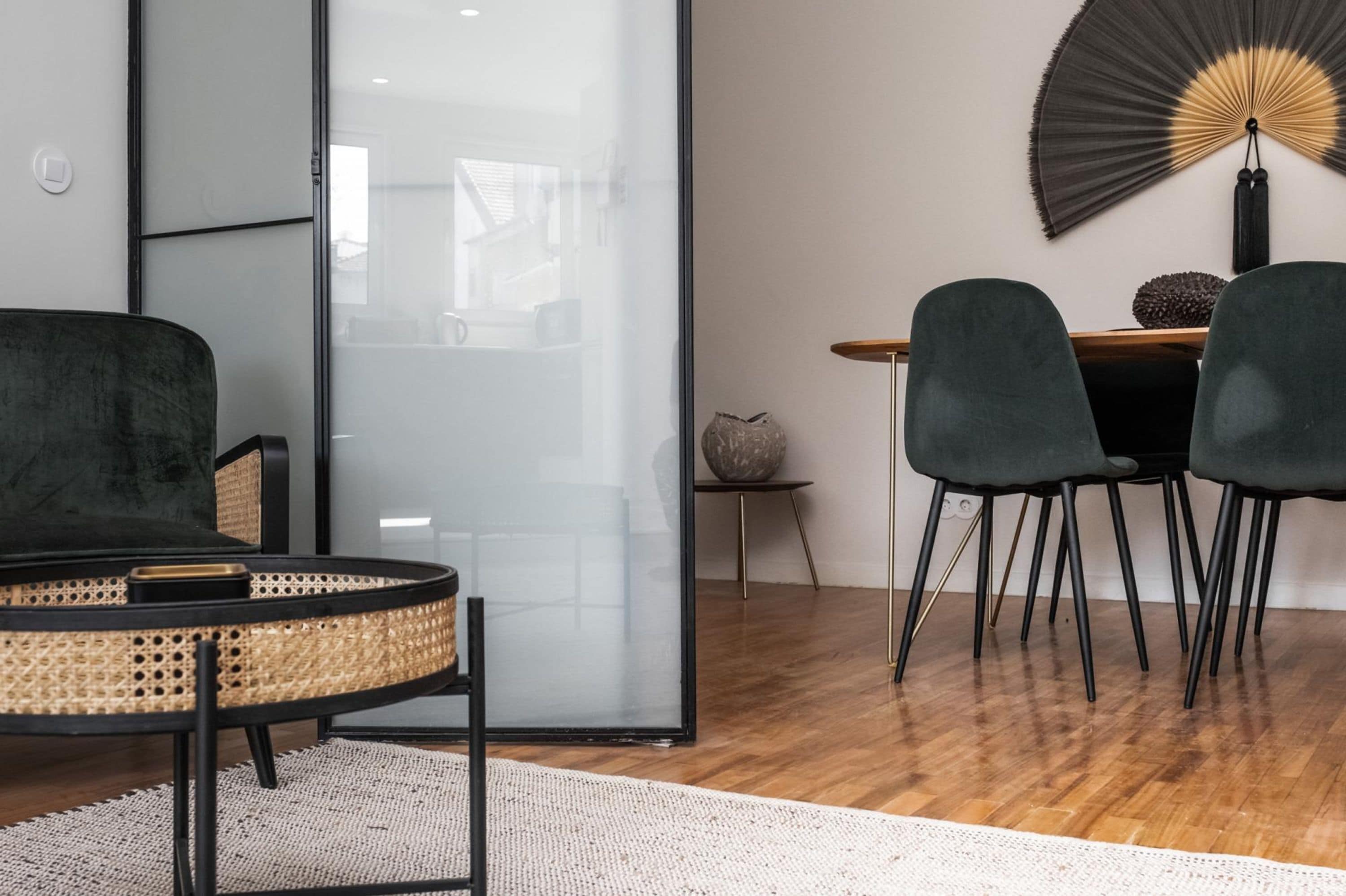 Uma sala de estar moderna com uma poltrona redonda de vime, um sofá escuro e uma área de jantar com duas cadeiras e uma mesa.