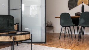 A modern living room with a round rattan chair, a dark sofa, and a dining area with two chairs and a table. - Nomad s By Sta Catarina Flats - 3bdr Family (Porto)