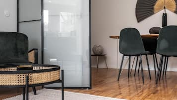 Uma sala de estar moderna com uma poltrona redonda de vime, um sofá escuro e uma área de jantar com duas cadeiras e uma mesa.