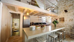 A modern kitchen with a large island, stone walls, and a loft area above. - Leonora House With Private Pool Close to Gaios (Paxos)