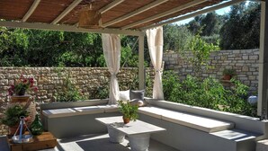 A covered outdoor seating area with stone walls, potted plants, and a stone bench. - Leonora House With Private Pool Close to Gaios (Paxos)