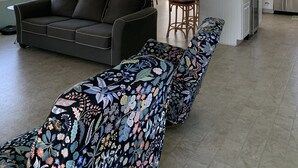 Amplia sala de estar con sofá, un banco estampado, una cocina con refrigerador y un comedor con sillas.